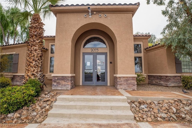 view of exterior entry with a tiled roof, stone siding, stucco siding, and french doors