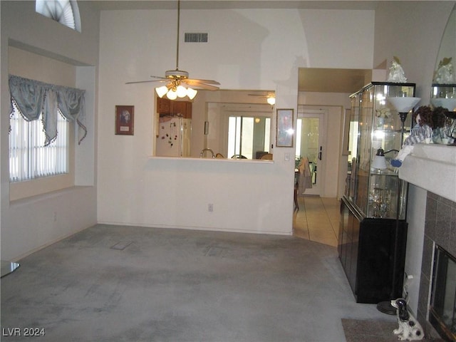 carpeted living room featuring a tile fireplace, a high ceiling, a wealth of natural light, and ceiling fan