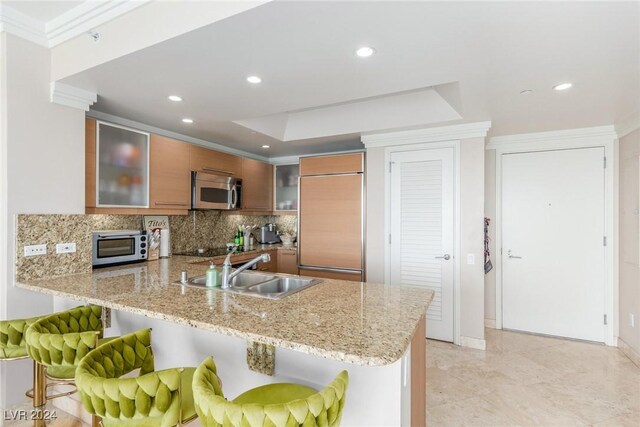 kitchen featuring sink, backsplash, a kitchen breakfast bar, paneled refrigerator, and kitchen peninsula