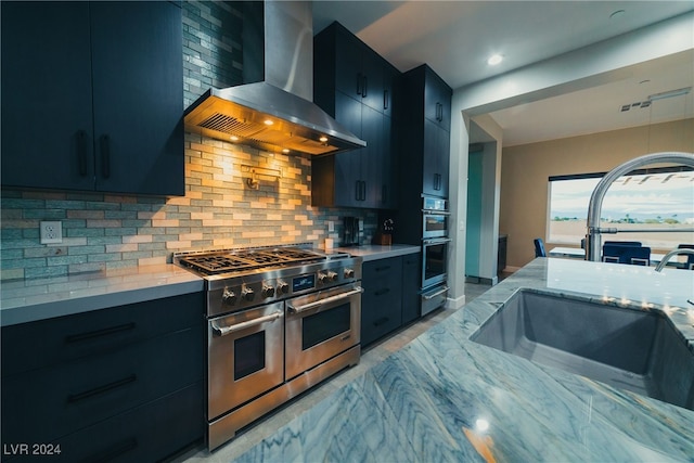 kitchen with sink, backsplash, range with two ovens, light stone counters, and wall chimney range hood