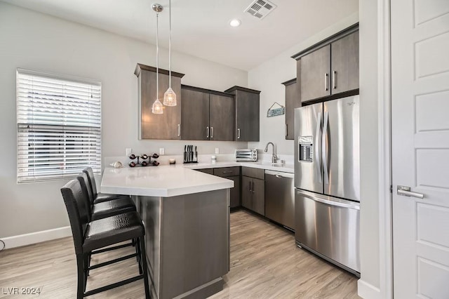 kitchen with light hardwood / wood-style flooring, appliances with stainless steel finishes, hanging light fixtures, a kitchen breakfast bar, and kitchen peninsula