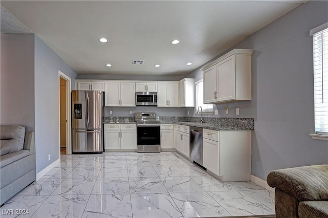 kitchen with stone countertops, a healthy amount of sunlight, white cabinetry, and stainless steel appliances