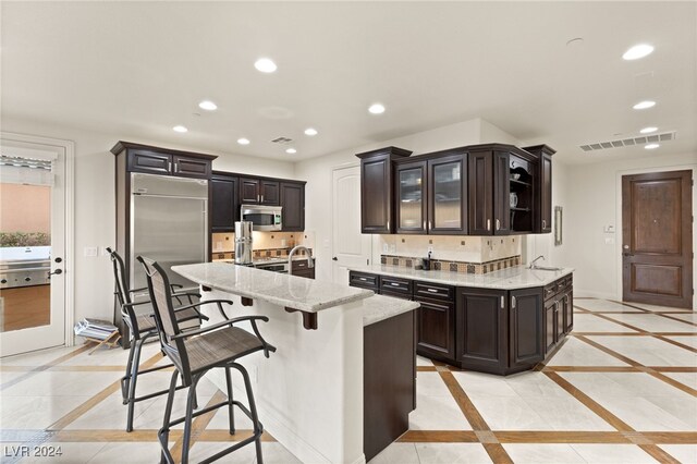 kitchen featuring recessed lighting, appliances with stainless steel finishes, glass insert cabinets, light stone countertops, and baseboards