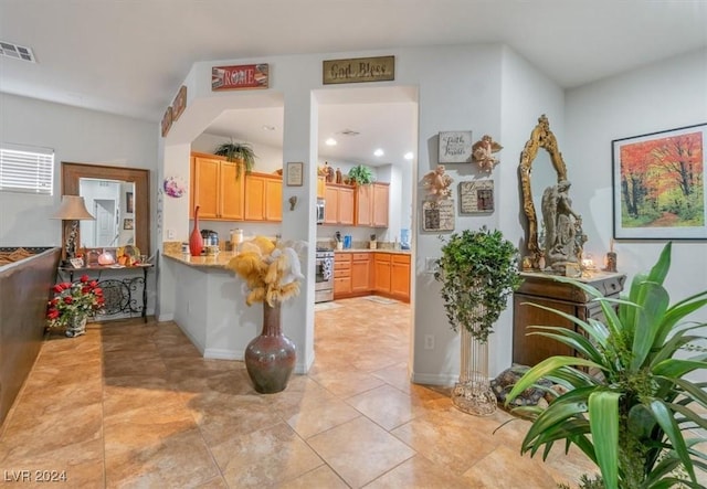 kitchen with light tile patterned floors, kitchen peninsula, stainless steel appliances, and light brown cabinetry