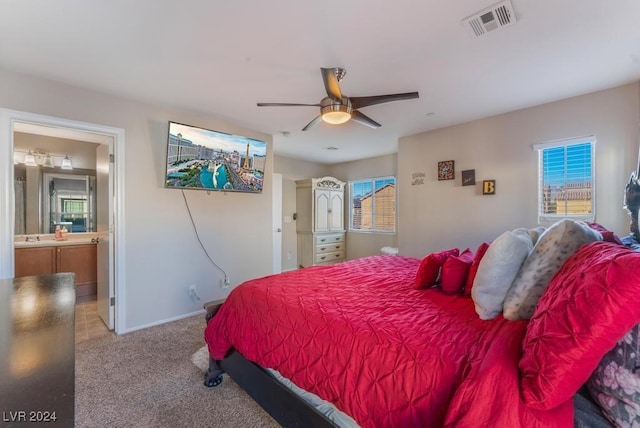 bedroom featuring multiple windows, connected bathroom, light carpet, and ceiling fan