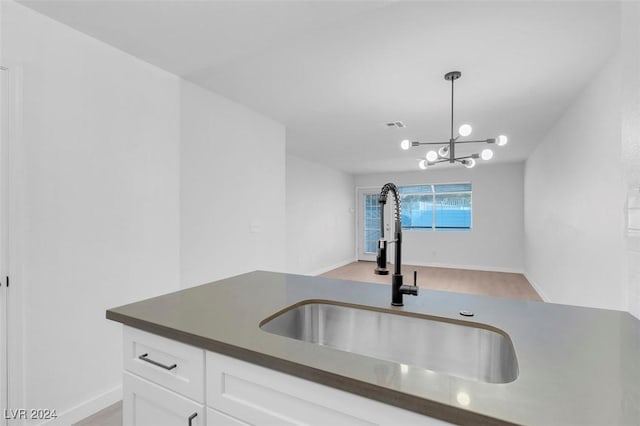 kitchen featuring pendant lighting, light hardwood / wood-style floors, white cabinetry, and sink