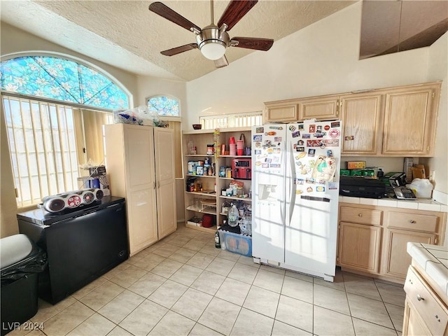 kitchen featuring white refrigerator with ice dispenser, vaulted ceiling, a textured ceiling, tile counters, and light tile patterned flooring