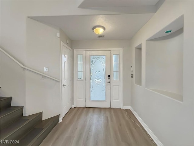 entrance foyer featuring baseboards, stairs, visible vents, and wood finished floors