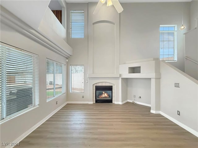 unfurnished living room featuring wood finished floors, a tile fireplace, a high ceiling, and baseboards