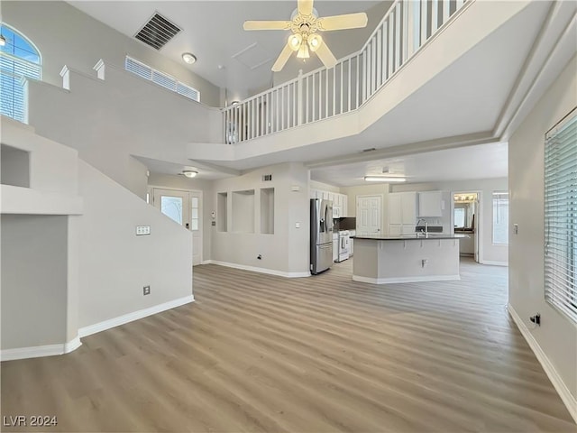 unfurnished living room featuring visible vents, a ceiling fan, a healthy amount of sunlight, light wood-type flooring, and baseboards