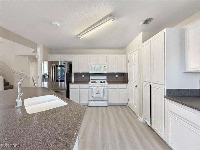 kitchen with dark countertops, white appliances, white cabinets, and a sink