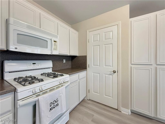 kitchen featuring tasteful backsplash, dark countertops, light wood-style floors, white cabinetry, and white appliances