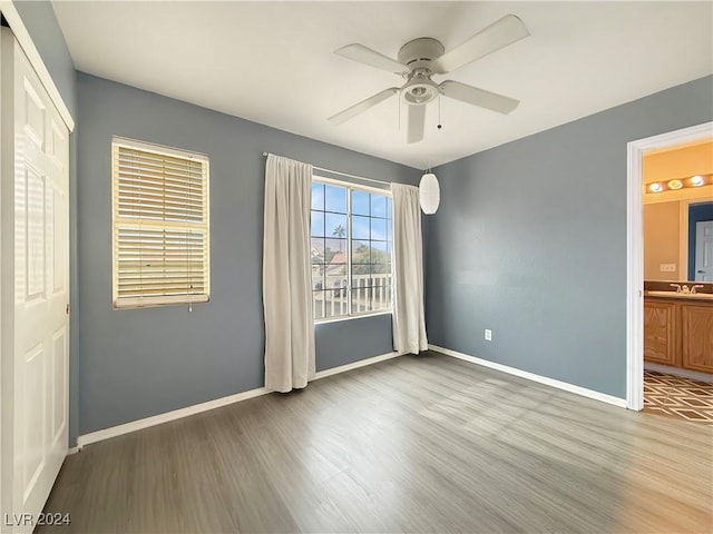 unfurnished bedroom with ensuite bathroom, ceiling fan, a sink, wood finished floors, and baseboards