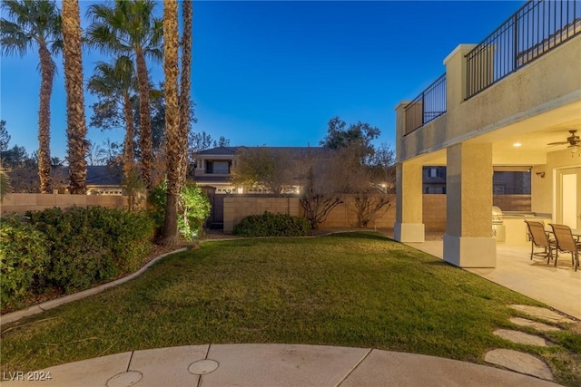 yard at dusk with a balcony, a patio, and an outdoor kitchen