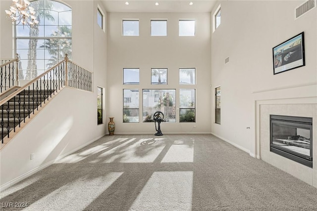 unfurnished living room with light colored carpet, a towering ceiling, a fireplace, and a chandelier