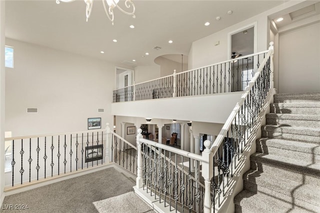 stairway with carpet flooring, a towering ceiling, and an inviting chandelier