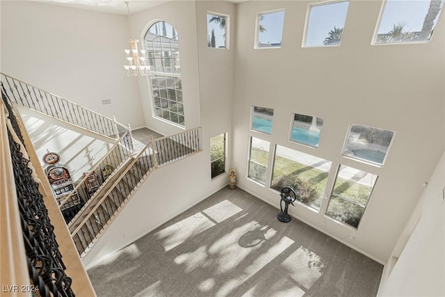 staircase featuring carpet flooring, a wealth of natural light, a towering ceiling, and an inviting chandelier