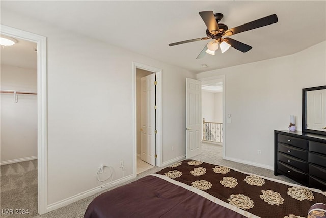 bedroom featuring a walk in closet, ceiling fan, a closet, and light colored carpet