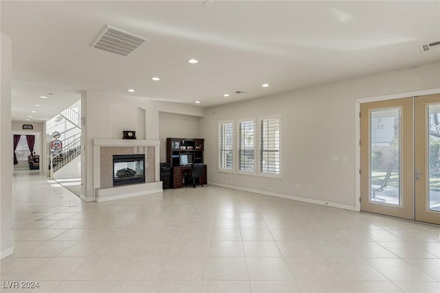 unfurnished living room with a multi sided fireplace, light tile patterned floors, and french doors