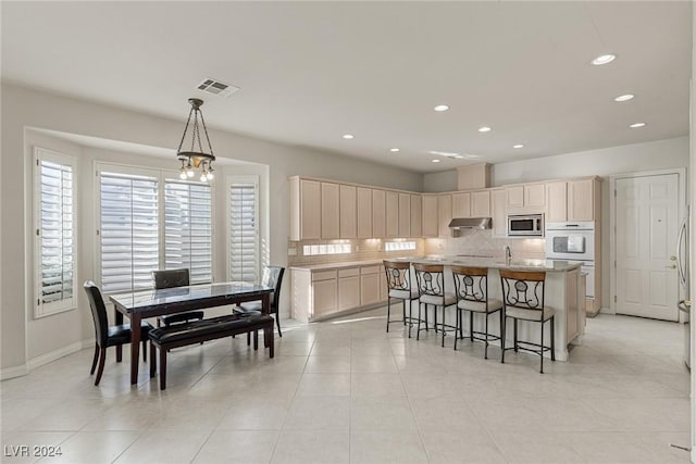 kitchen featuring stainless steel microwave, a kitchen island with sink, hanging light fixtures, light tile patterned floors, and a notable chandelier