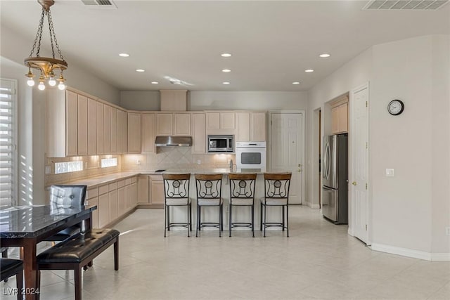 kitchen with light brown cabinets, a breakfast bar area, a kitchen island, stainless steel appliances, and a chandelier