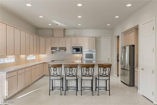 kitchen with light brown cabinets, a kitchen island with sink, light tile patterned floors, a kitchen bar, and stainless steel appliances