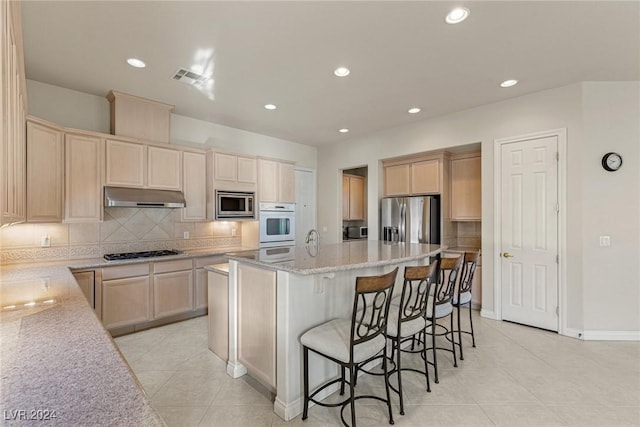 kitchen featuring tasteful backsplash, light stone counters, a kitchen island with sink, light tile patterned floors, and appliances with stainless steel finishes