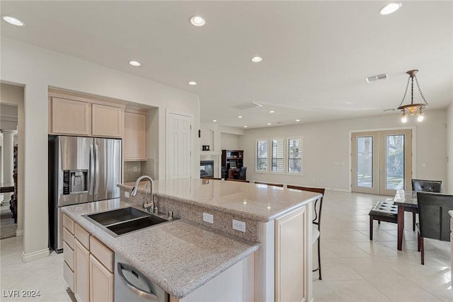 kitchen with light stone countertops, appliances with stainless steel finishes, sink, a center island with sink, and a chandelier