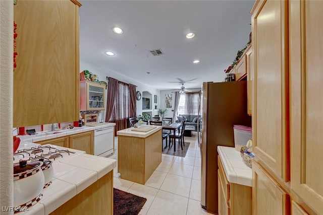 kitchen featuring ceiling fan, dishwasher, a center island, stainless steel refrigerator, and tile counters