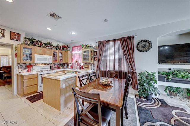 kitchen featuring a center island, white appliances, backsplash, light tile patterned floors, and light brown cabinetry