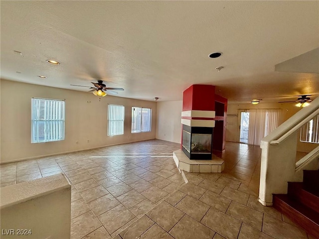 unfurnished living room with a tile fireplace, ceiling fan, light tile patterned flooring, and a textured ceiling