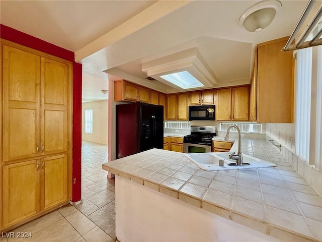 kitchen with sink, kitchen peninsula, tile countertops, light tile patterned floors, and black appliances