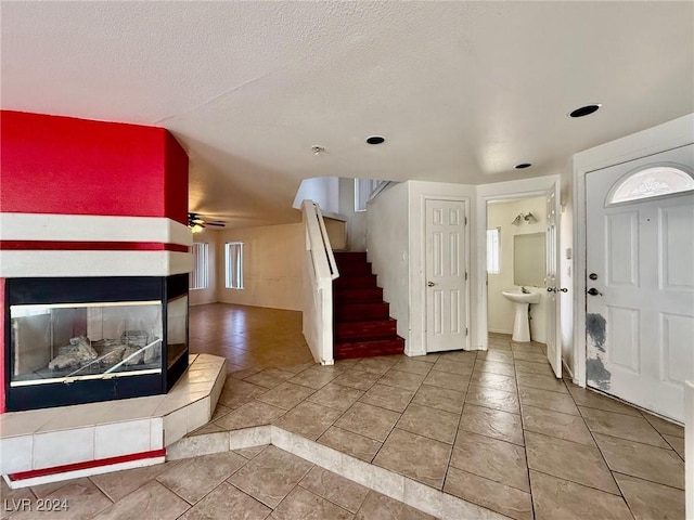 entryway featuring a fireplace, a textured ceiling, tile patterned floors, and ceiling fan