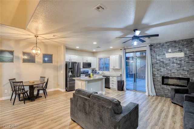 living room featuring a textured ceiling, a fireplace, light hardwood / wood-style floors, and ceiling fan with notable chandelier