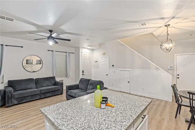 kitchen with decorative light fixtures, light hardwood / wood-style floors, light stone countertops, and ceiling fan with notable chandelier