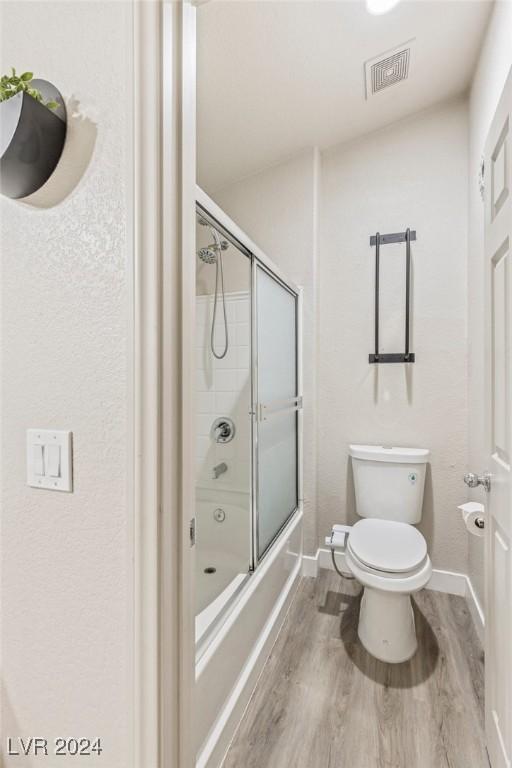 bathroom featuring toilet, combined bath / shower with glass door, and hardwood / wood-style flooring