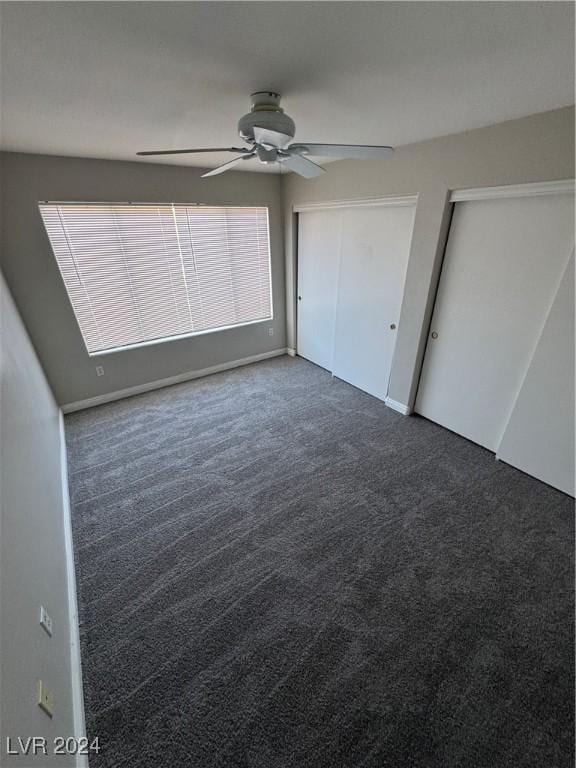 unfurnished bedroom with dark carpet, ceiling fan, and multiple closets