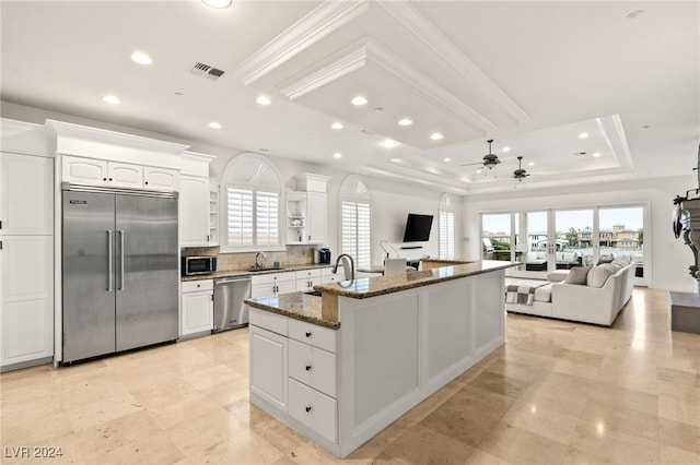 kitchen featuring appliances with stainless steel finishes, dark stone counters, sink, a center island with sink, and white cabinetry