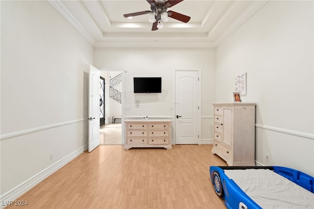 unfurnished bedroom featuring light wood-type flooring, a raised ceiling, ceiling fan, and crown molding