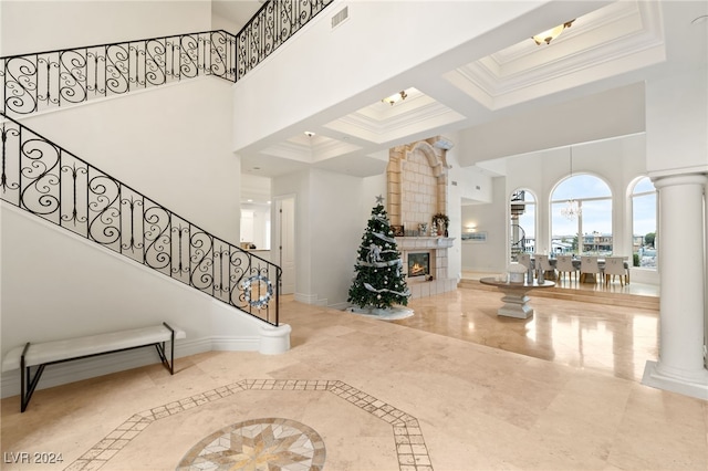 entryway featuring a towering ceiling, a large fireplace, ornamental molding, and coffered ceiling