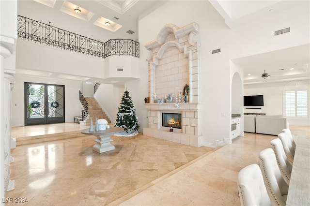 living room with a fireplace, french doors, a towering ceiling, and ornamental molding