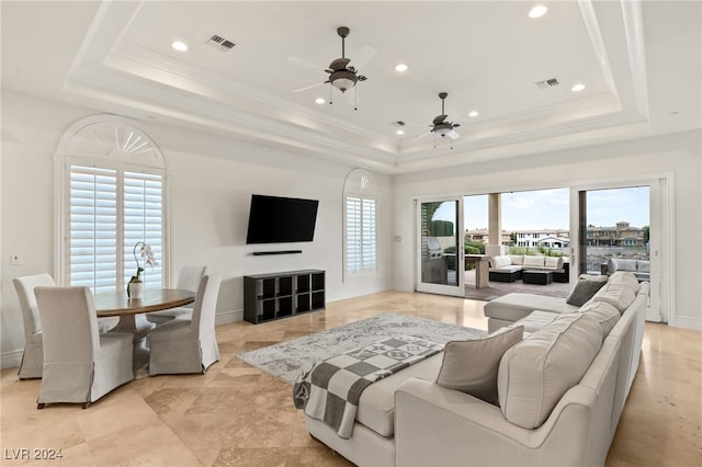 living room featuring a raised ceiling, ceiling fan, and plenty of natural light