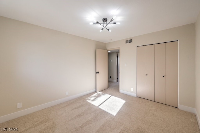 unfurnished bedroom with a chandelier, light colored carpet, and a closet