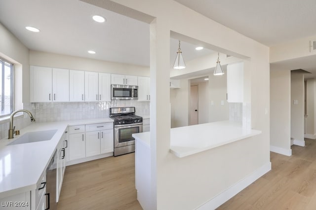 kitchen featuring white cabinetry, sink, light hardwood / wood-style flooring, decorative light fixtures, and appliances with stainless steel finishes