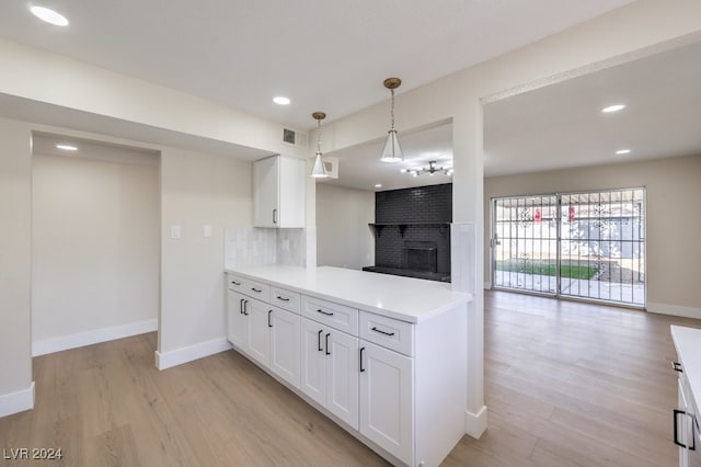 kitchen featuring white cabinets, light hardwood / wood-style flooring, a fireplace, decorative light fixtures, and kitchen peninsula