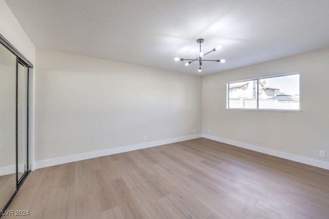 empty room with an inviting chandelier, a textured ceiling, and light wood-type flooring