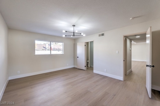 spare room with a chandelier, a textured ceiling, and light hardwood / wood-style flooring