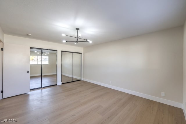 unfurnished bedroom featuring a chandelier, light wood-type flooring, and multiple closets