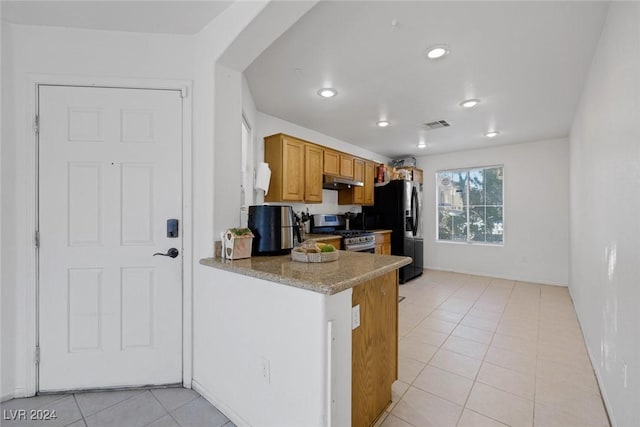 kitchen with stone counters, light tile patterned floors, black refrigerator with ice dispenser, and stainless steel range with gas stovetop