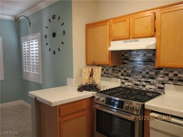 kitchen with tile counters, stainless steel range, tile patterned flooring, backsplash, and ornamental molding